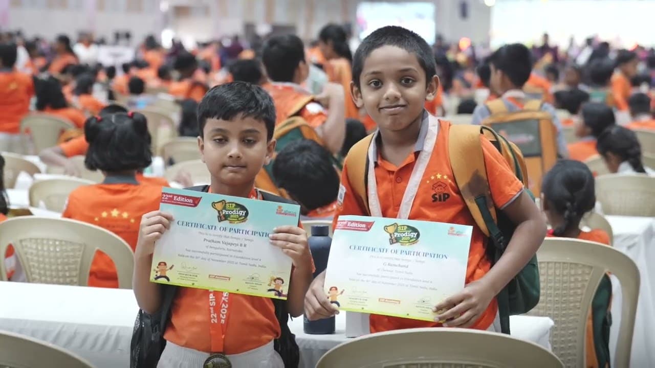 Two SIP Abacus students holding certificates in a hall packed with children in orange